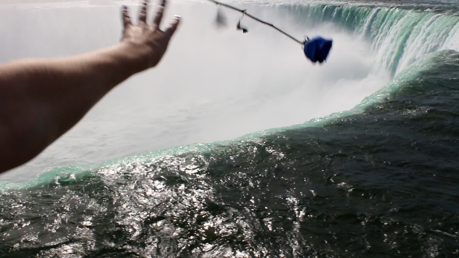 a hand tossing a blue rose over the niagara falls. video still